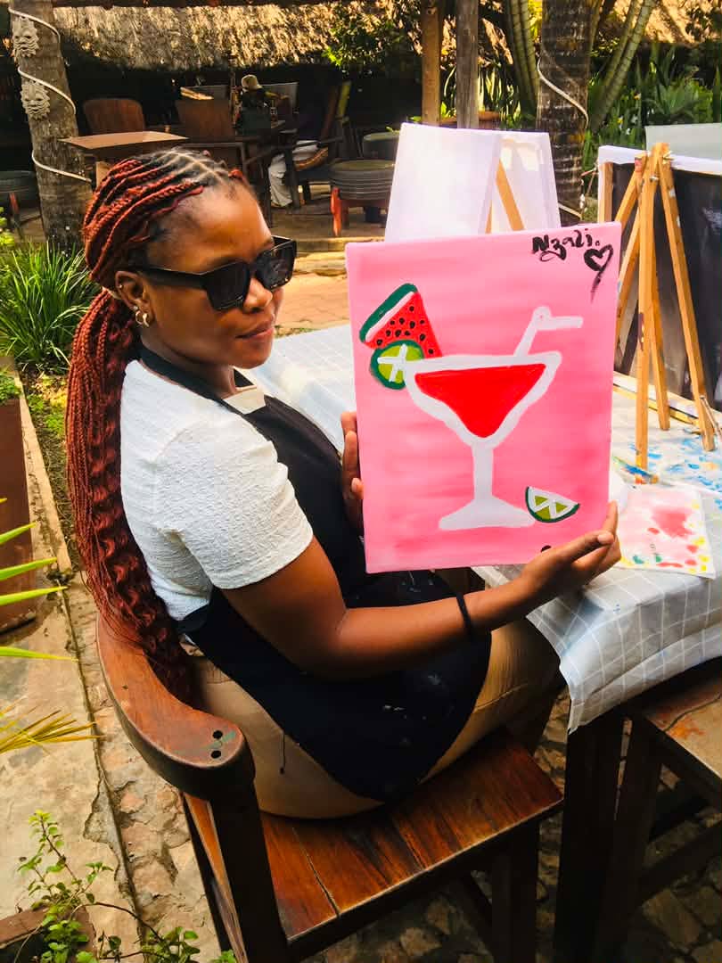 A guest holding up her finished cocktail painting