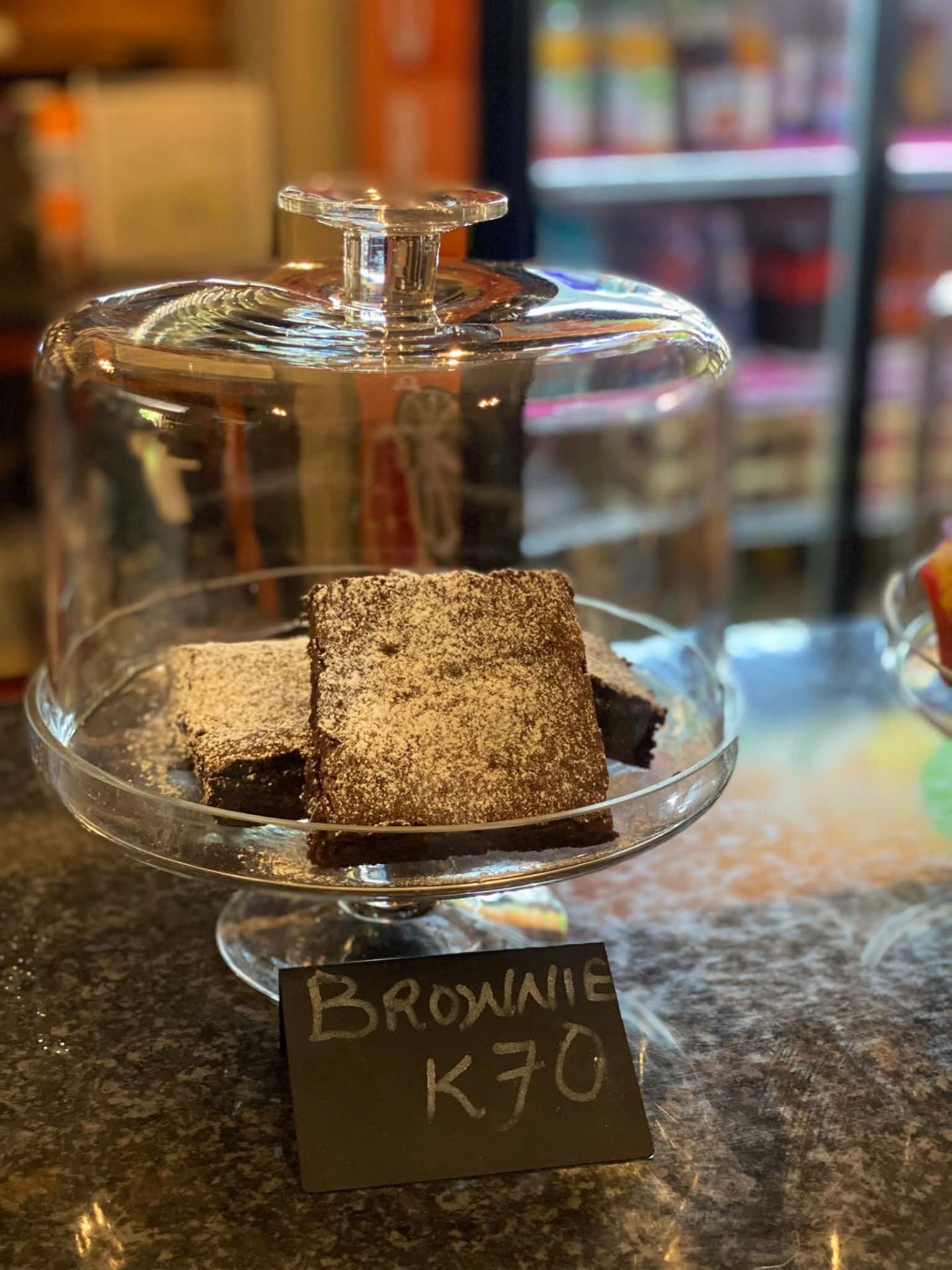 Dusted chocolate brownies under a glass cake dome