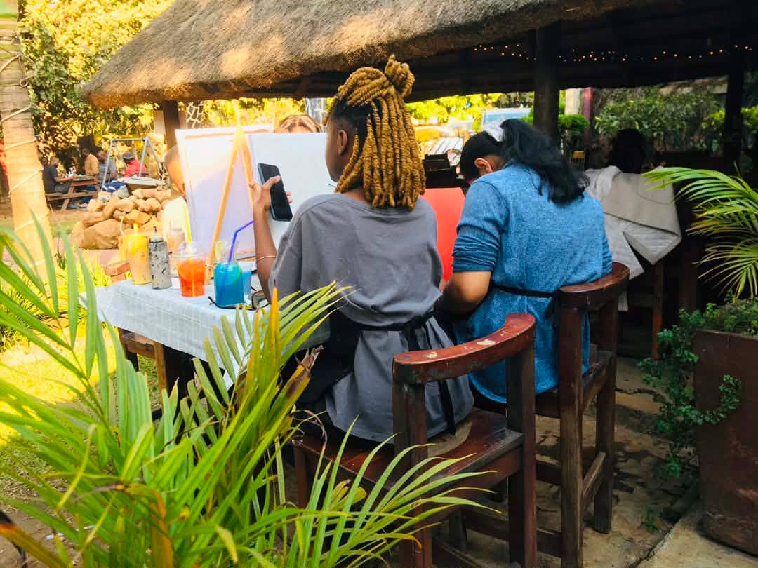 Guests painting side by side at easels under the thatched hut